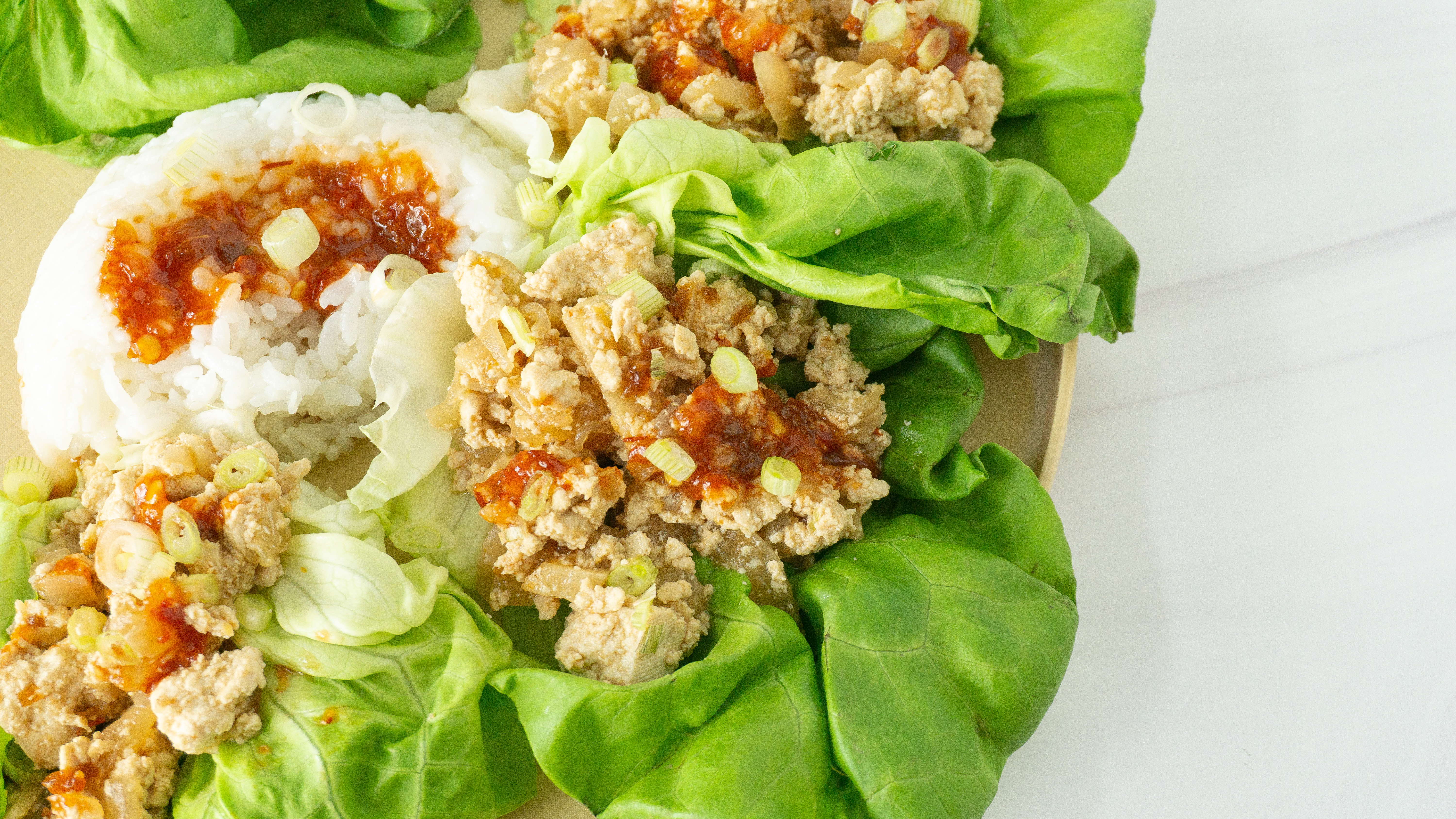 three tofu lettuce wraps on a place with white basmati rice and sauce drizzled over the top